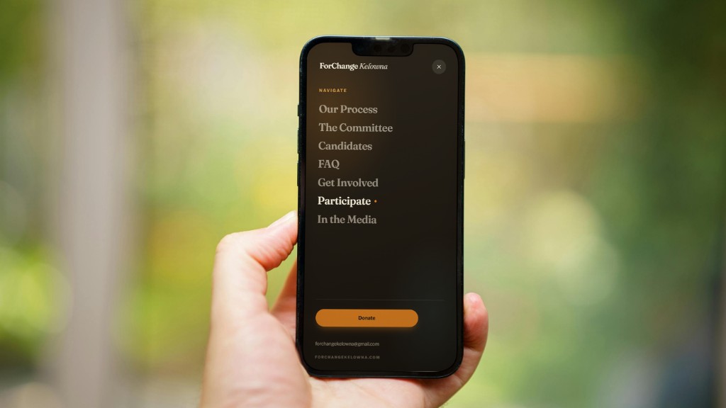 Phone in a hand showing the ForChange Kelowna dark-mode mobile menu